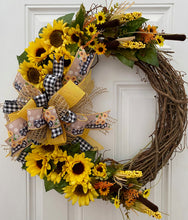 Load image into Gallery viewer, Our beautifully put-together Sunflower Smile wreath measures 24" in diameter. It is creatively decorated with silk sunflowers, greens, cattails, corn, flowers, and a variety of ribbons including a yellow burlap, black & white checkered, lattice ribbon, and the "ole vintage truck with sunflowers" in its ribbon. There are cork surface protectors on the back so your door/wall will be protected.