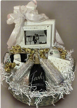 Load image into Gallery viewer, Pop the bubbly and let the cheers echo, for this basket holds a bottle of Prosecco and two stemless flutes, ready to clink in honor of love's grand adventure. A beautiful wedding-themed picture frame speaks volumes, a sweet reminder of the love story they're just beginning to write. And oh, the indulgence! Chocolates to make hearts flutter, lotion for tender care, and a scented candle to set the mood. This isn't just a gift; it's a ticket to a love-filled journey down memory lane, a keepsake of their