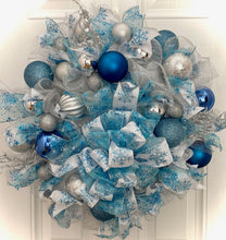 Load image into Gallery viewer, Step into a world of frosty elegance with this enchanting handmade wreath! Crafted with shimmering white and silver mesh, adorned with an assortment of dazzling blue and silver ornament balls, and accentuated by the whimsical charm of snowflake-themed ribbon, this wreath is a celebration of all things merry and bright! Embrace the winter wonderland vibes as this 26-inch masterpiece dazzles any space it graces.