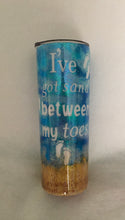 Load image into Gallery viewer, &quot;I&#39;ve got sand between my toes&quot; is a 20-ounce skinny tumbler that is a bit more slender than a regular 20-ounce cup. This particular cup is a beach theme made with inking technique, vinyl, glitter, and extra fine sand. It is handmade and is stainless steel and great for any hot or cold drinks. It comes with a lid and can be personalized for him/her. We can add this tumbler to a gift basket as well.