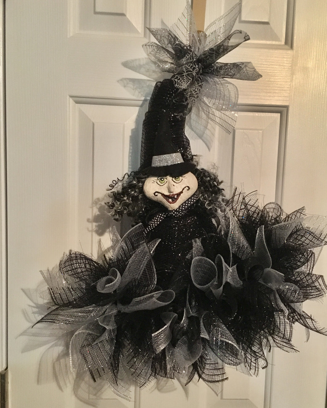 Witchie Witch... Oh, My is a handmade witch hat with this scary witch face that will surely decorate your door or wall for Halloween!  Made with a black and silver mesh mix and embellished with silver glitz for that special Halloween welcome. It measures approximately 24